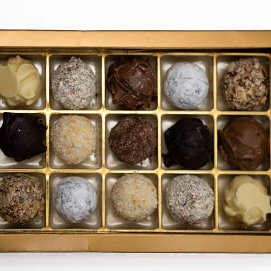 Nahaufnahme von 15 handgefüllten Sahne-Trüffeln. in einer goldenen Einlage.